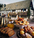 Bread and pastries laid out on a table with a timber-framed house in the background